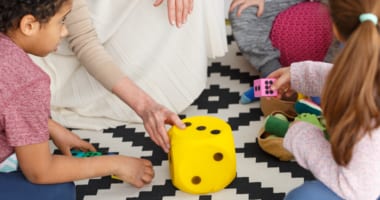 Big yellow plush dice on a carpet in a classroom with students