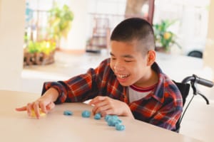 Asian child in a wheelchair interacting with yellow and blue modeling clay.