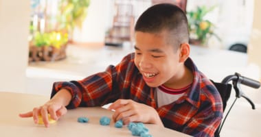 Child in a wheelchair interacting with yellow and blue modeling clay.
