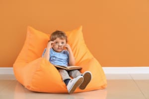 Young white boy with glasses and book sitting on a beanbag chair.