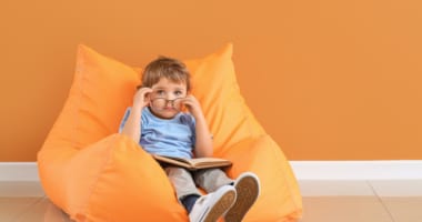 Child with glasses and book sitting on a beanbag chair.