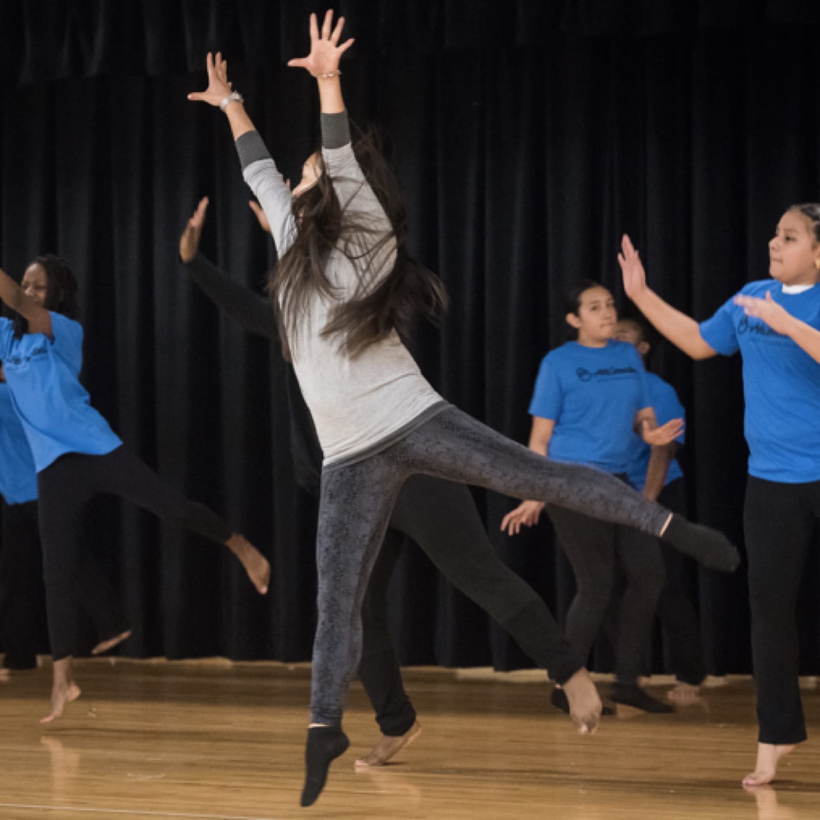 Teaching artist models a leaping dance move for students, following behind.