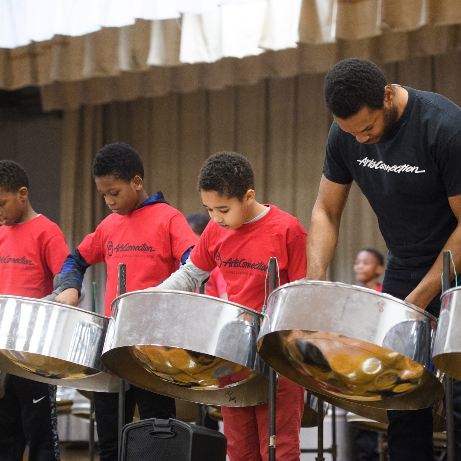 A teacher and three students stand on stage playing the steel drum