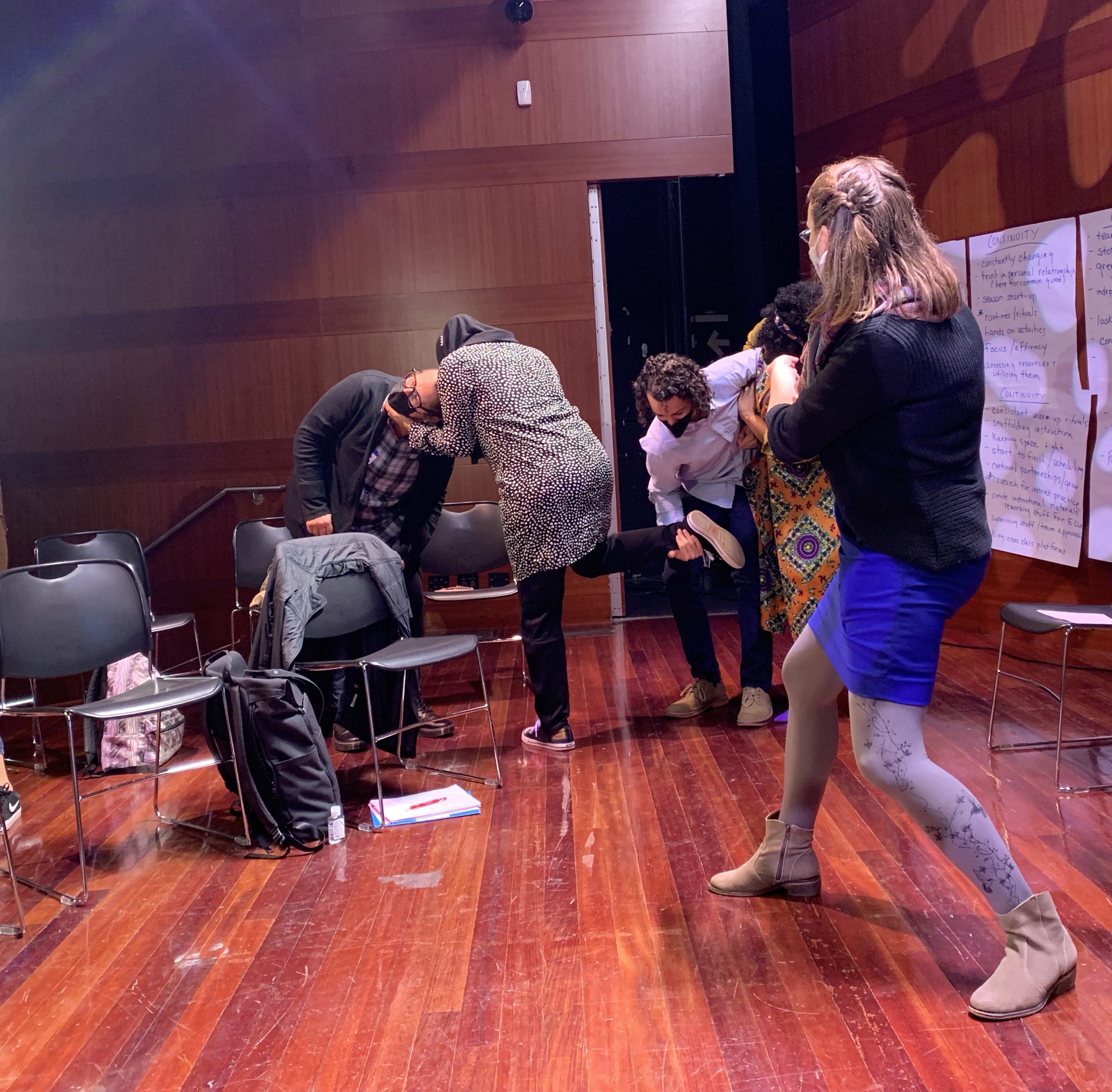 Photograph of four adults creating tableau while a facilitator observes.