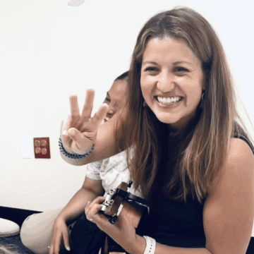 A photo of Carolyn smiling holding a camera in on hand and three finger up in the other.