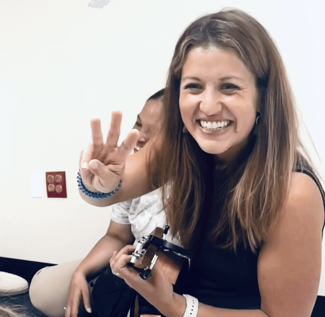 A photo of Carolyn smiling holding a camera in on hand and three finger up in the other.